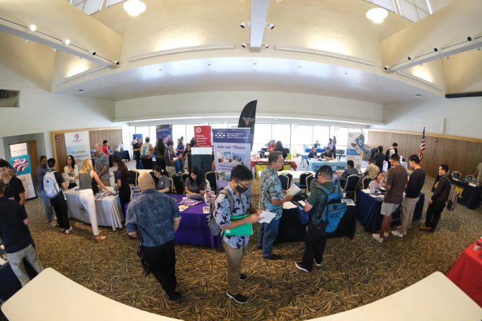 Dozens of participants visiting tables at a career fair in a ballroom.