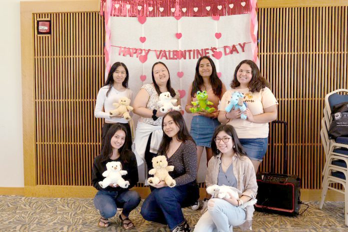 Students holding stuffed animals and posing in front of a banner that says: Happy Valentineʻs Day.