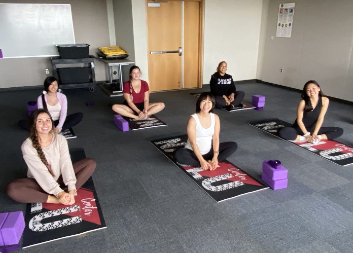 Six people sitting on mats in a room and doing yoga.