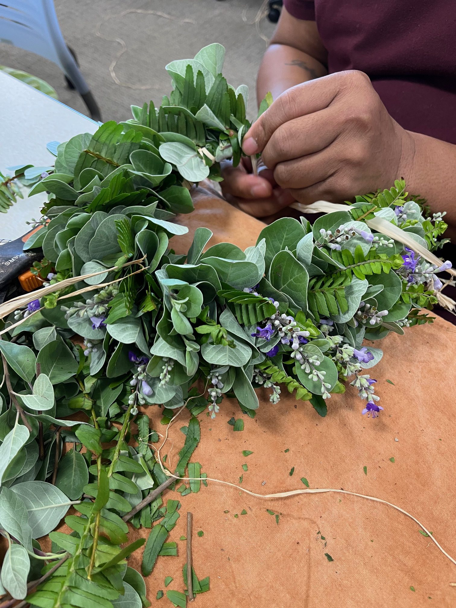 Closeup of hands making a head lei with various plant material.