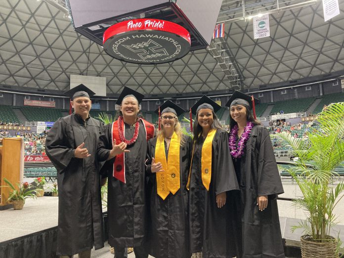 Students wearing graduation caps and gowns and standing inside an arena. They are smiling and posing for a group photo.
