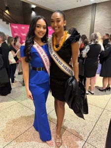 Two women wearing pageant sashes and posing for a photo.