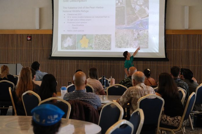 A student pointing to an image on a large screen with an audience watches.