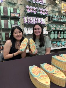 Two women sitting at a table and each holding up surfboard-shaped cookie tins.