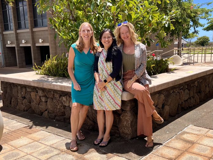 Three women standing outdoors and smiling for a group photo.