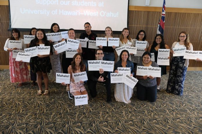 Students smiling and holding signs at the front of a ballroom.