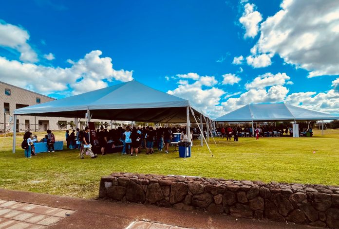 Students gathered under two tents on a lawn.