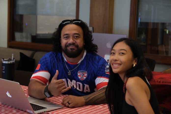 A man and woman sitting at a table with a laptop and smiling.