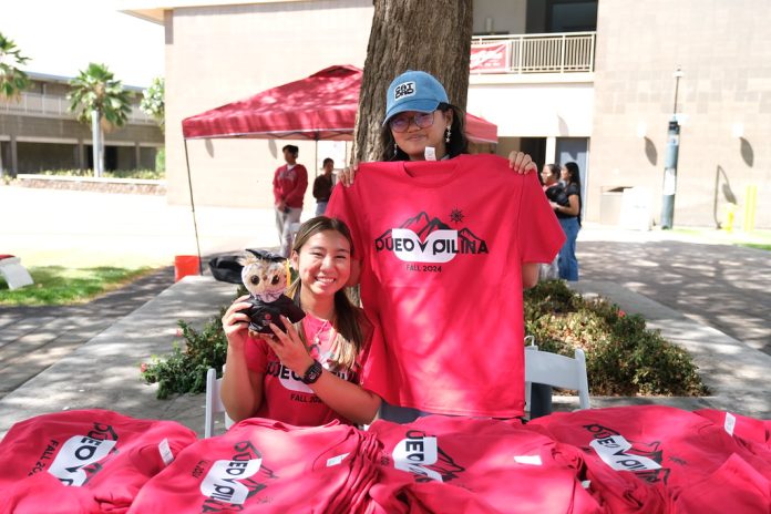 Two people smilng behind a table of red T-shirts.