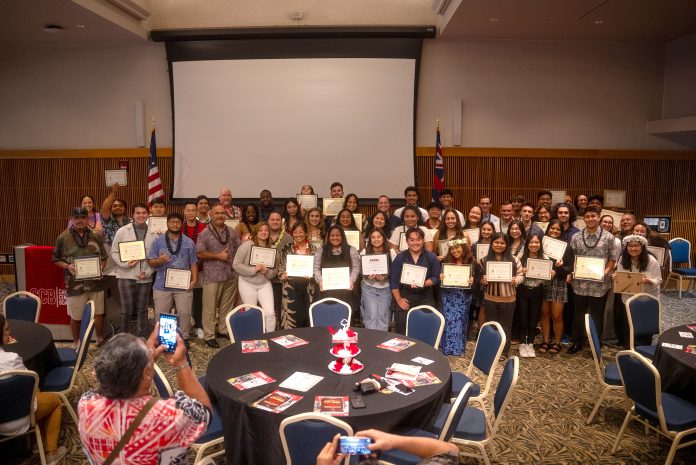 A group of men and women sitting and standing, holding award certificates, and posing for a group photo.