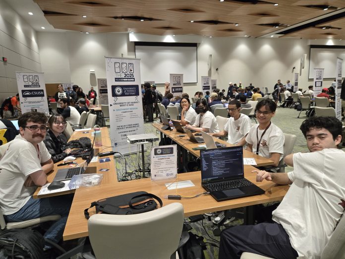 A group of students sitting at a large table with laptops in front of them.
