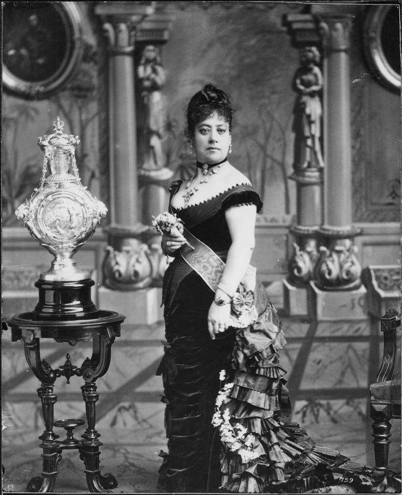 An image of Queen Emma standing in a room with ornate furnishings.