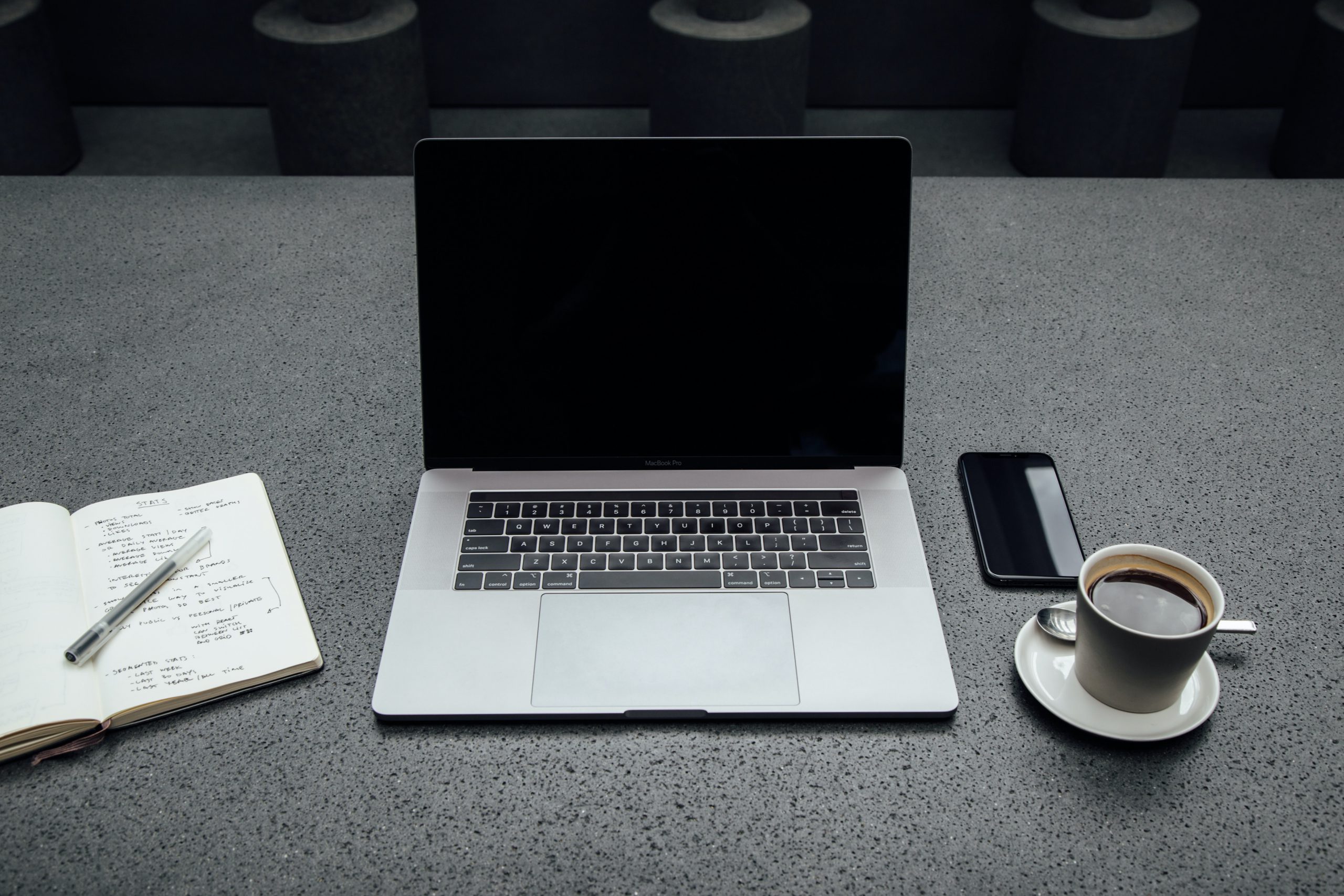 A picture of a workspace that has a laptop, smart phone, notebook, and cup of coffee.