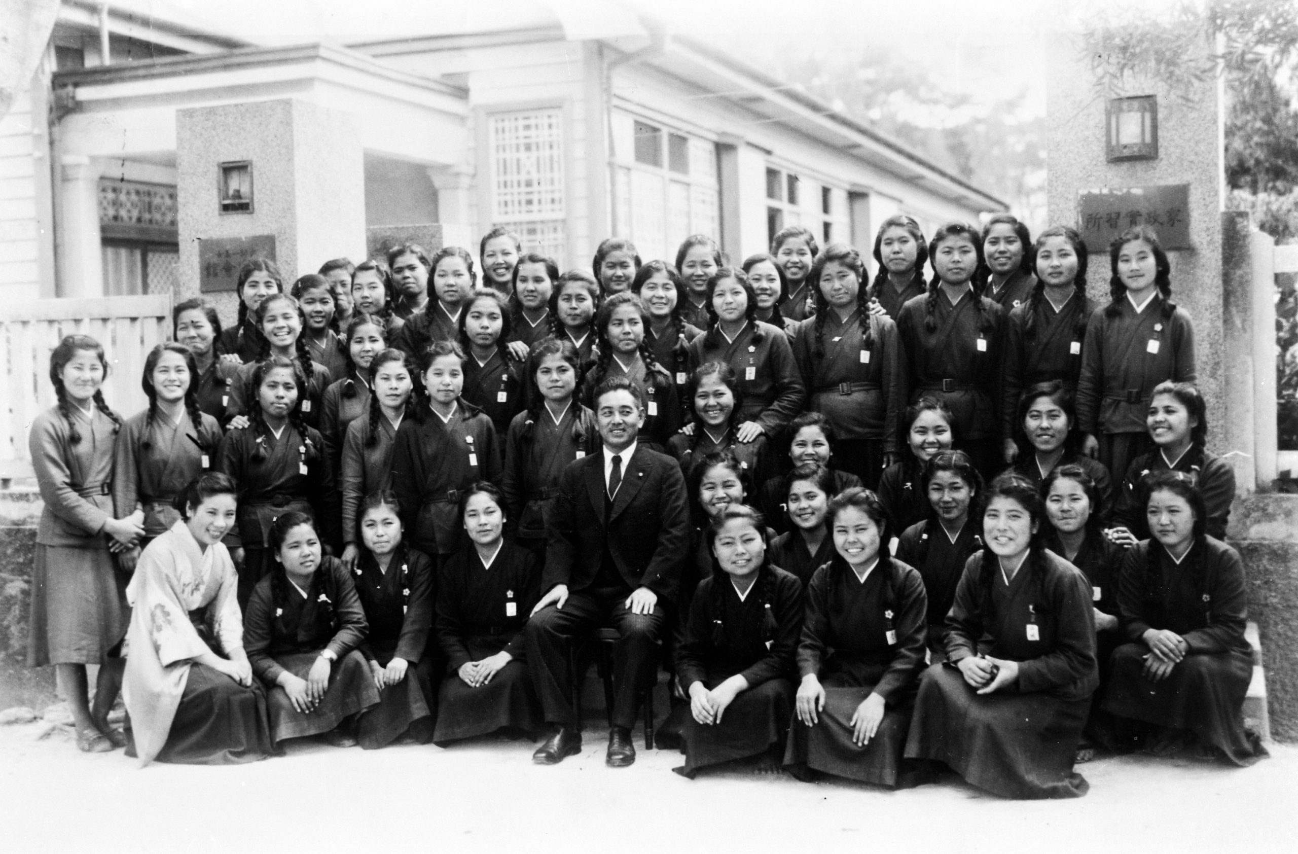 A large group of female students, otherwise known as the Himeyuri, standing behind Principal Noda at a closing-of-the-school-year ceremony.