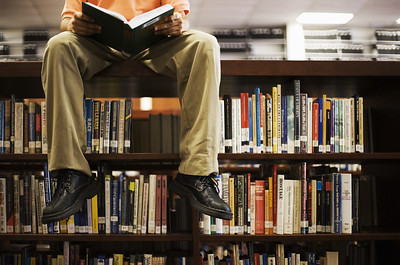 a man reading while sitting on a shelf