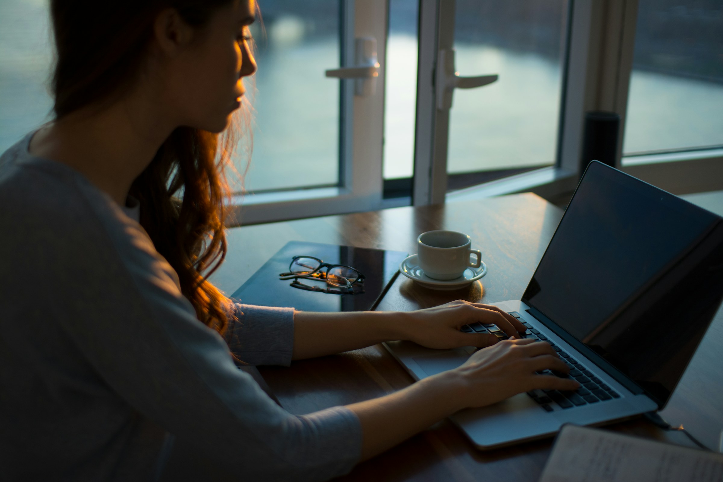 A person with long hair typing on a laptop in a dark room.