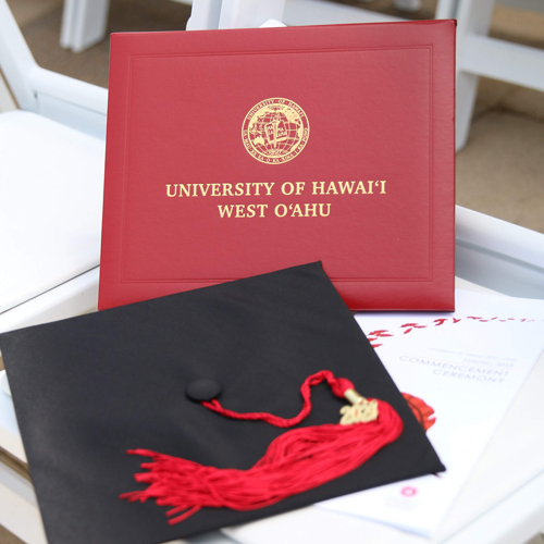 UHWO diploma cover with graduation cap on a white commencement chair.