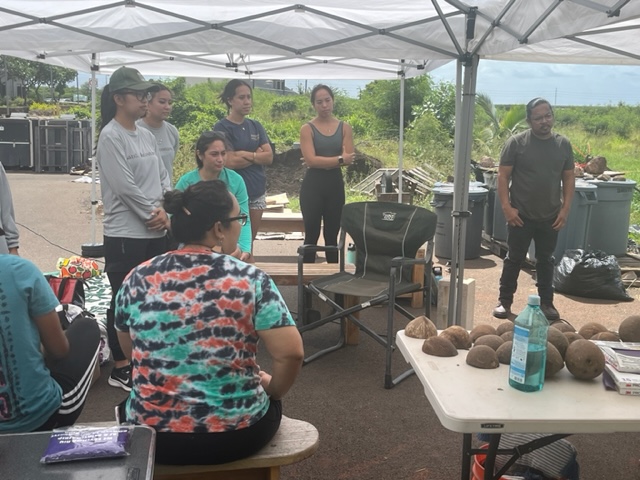 A group of men and women standing under a tent outdoors.