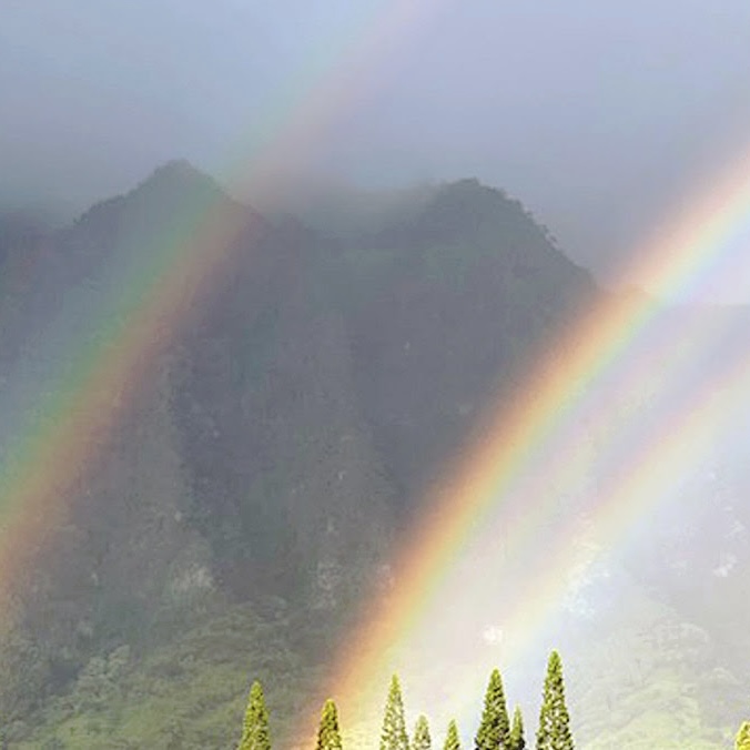 A double rainbow with green mountains in the background.
