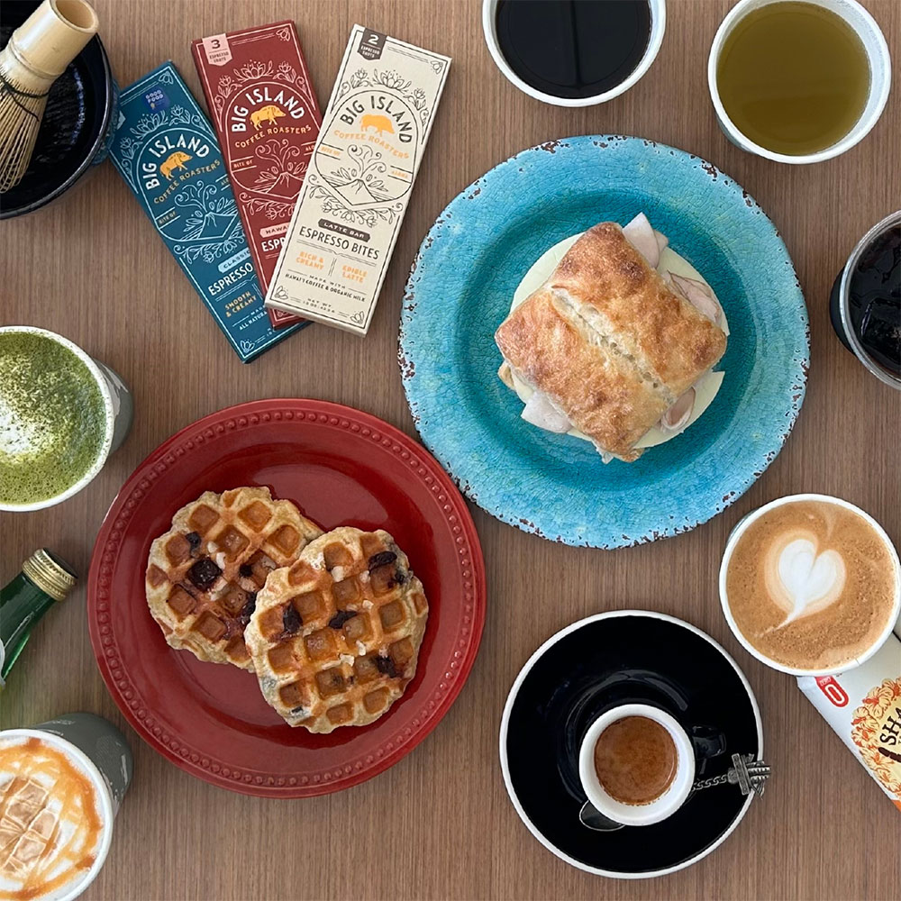 Tabletop with various coffees, waffles, and a sandwich.