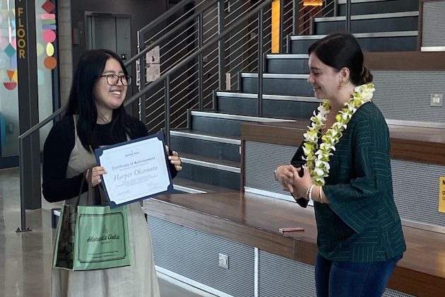 Two women, one holding a certificate and another wearing a lei.