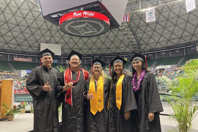 Students wearing graduation caps and gowns and standing inside an arena. They are smiling and posing for a group photo.