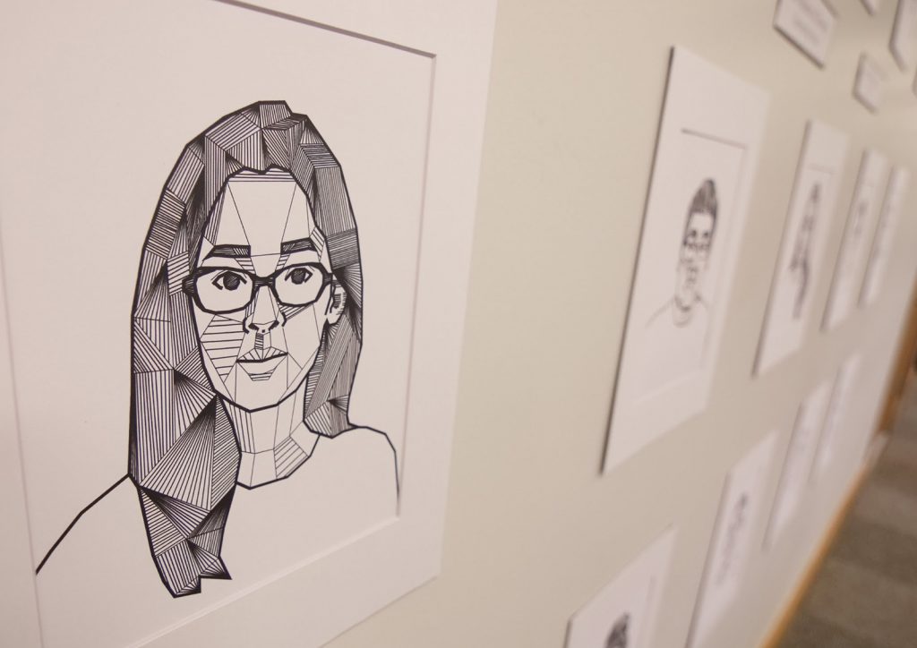 Hand-drawn images of student's faces hung on wall for display.