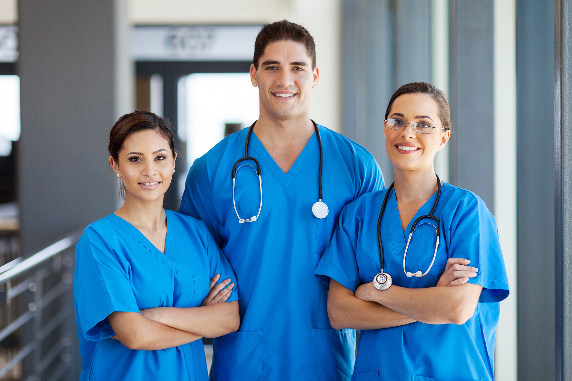 Three nurses in blue scrubs standing in a hallway.
