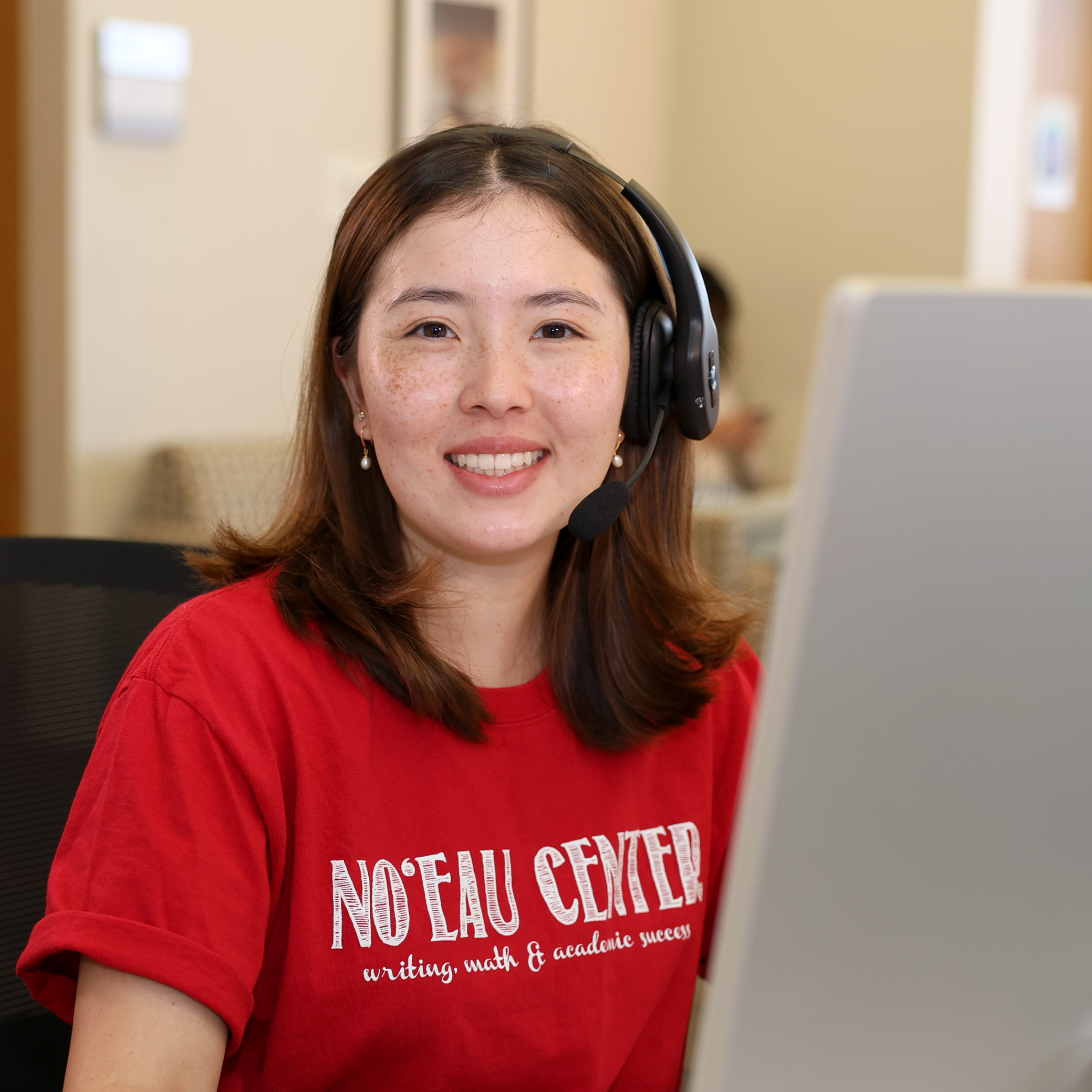 A No‘eau Center staff member sitting at the front desk wearing a headset.