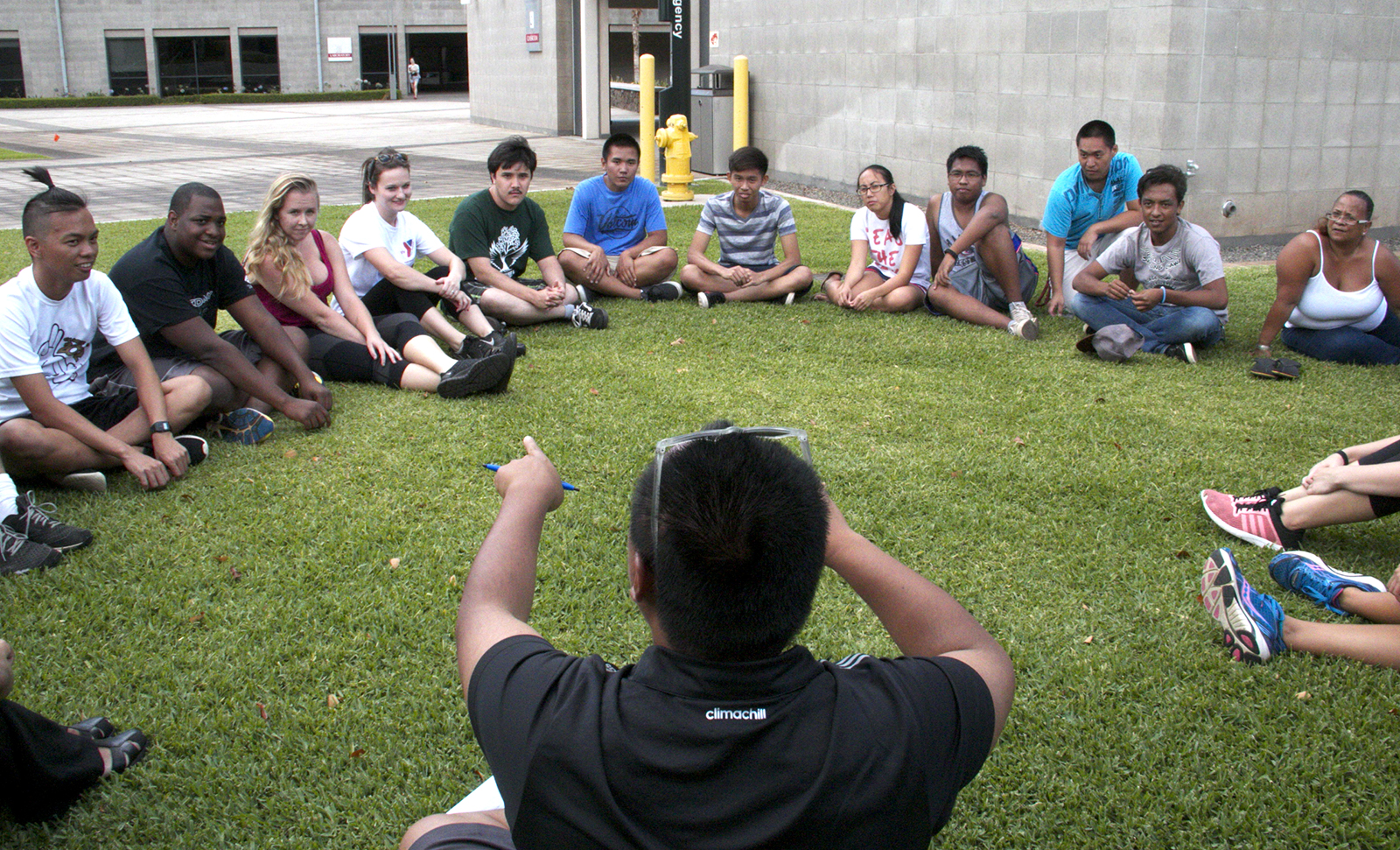 A instructor leading a large group sitting in a circle in the grass.