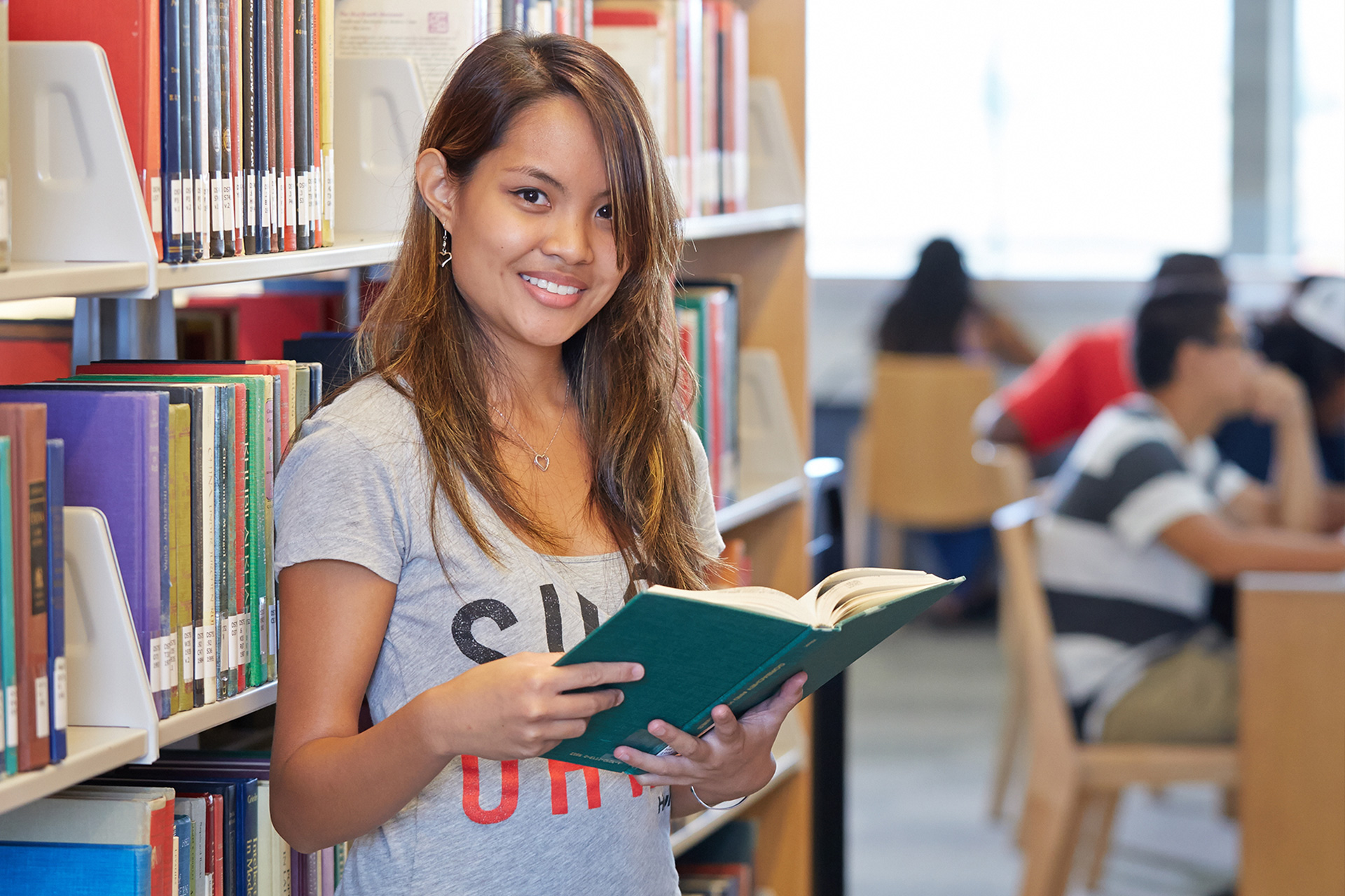 A student holding an open book in the library stacks.