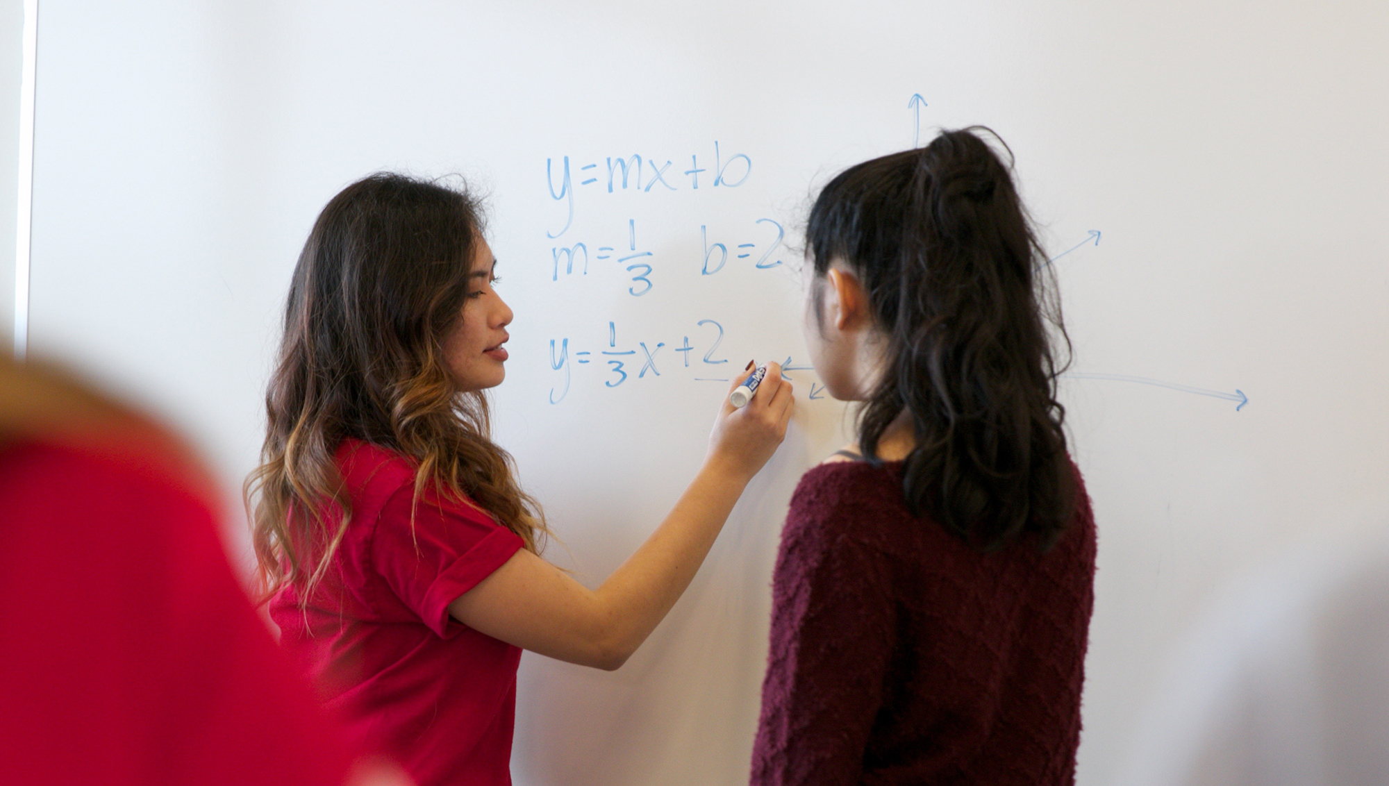 A tutor helping a student at a dry erase board with a math problem.