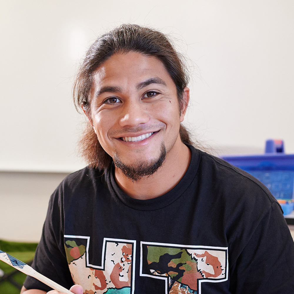 Close-up of a student smiling in a classroom with a black t-shirt.
