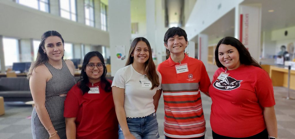 Five students pose together, smiling and wearing red shirts.