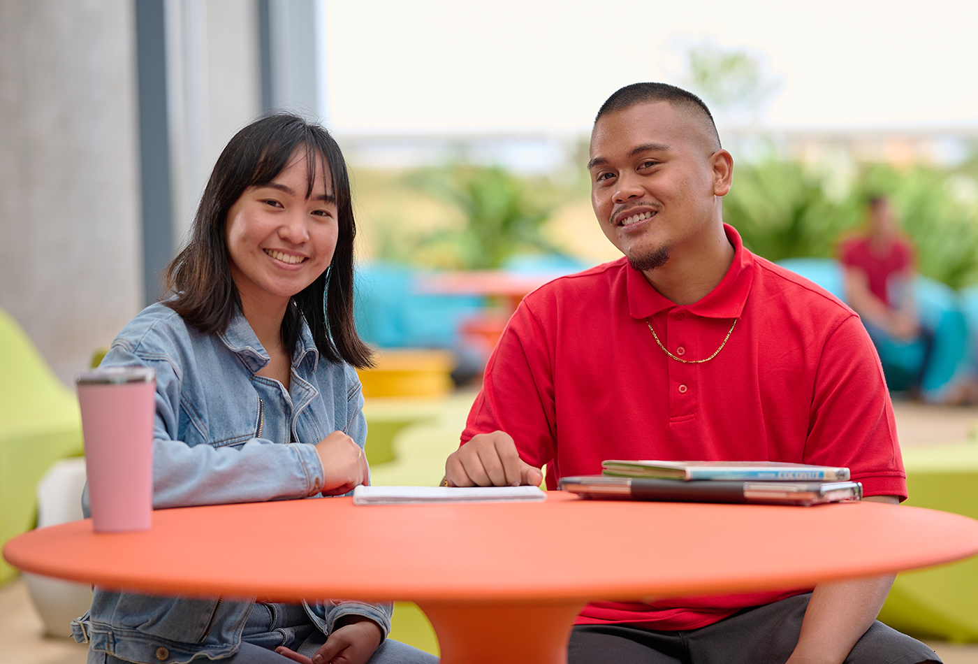 Two students sitting together at an orange table outside of the ACM building.